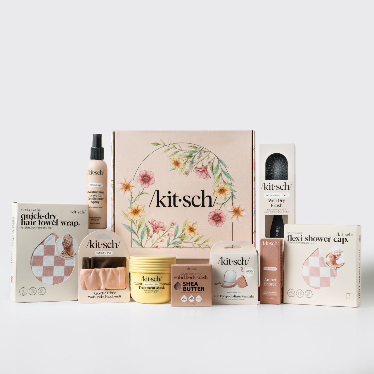 KITSCH Mother's Day Box gift set flat lay — pink floral /kit·sch/ gift box surrounded by all included products: Extra Large Quick-Dry Hair Towel Wrap, Moisturizing Leave-In Conditioner Spray with Argan Milk, Recycled Fabric Wide Twist Headbands, Treatment Mask with Coconut Oil, Shea Butter Solid Body Wash, LED Compact Mirror Keychain, Detangling Wet/Dry Brush, Amber Shores Hair Perfume, and Satin-Lined Flexi Shower Cap — Mother's Day hair & beauty gift set