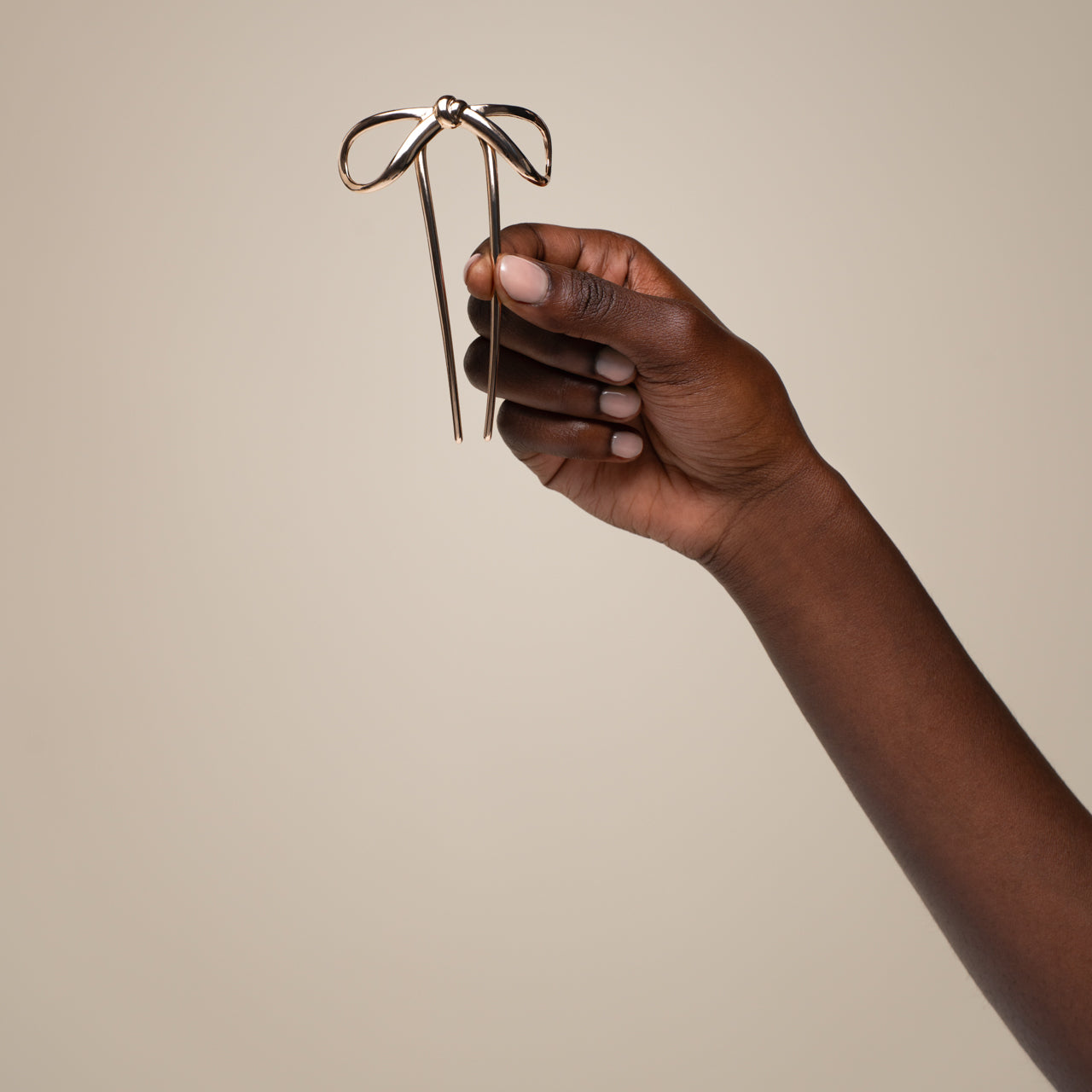 Hand holding a gold bow-shaped french hair pin against a beige background