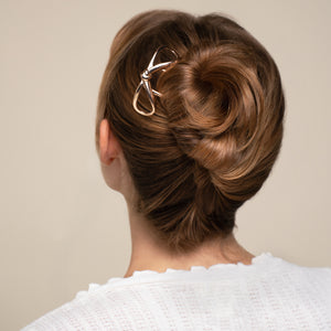 Woman with styled hair bun wearing a white sweater against a beige background