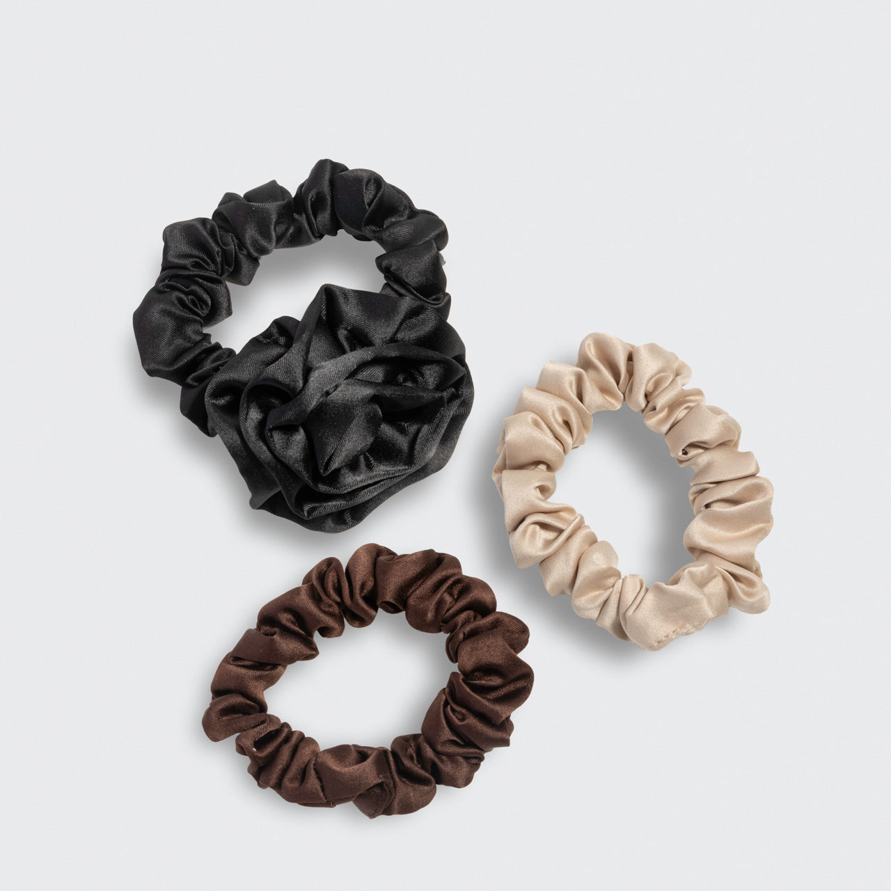 Three scrunchies with the black rosette and  brown and cream ruched scrunchies on a light gray background