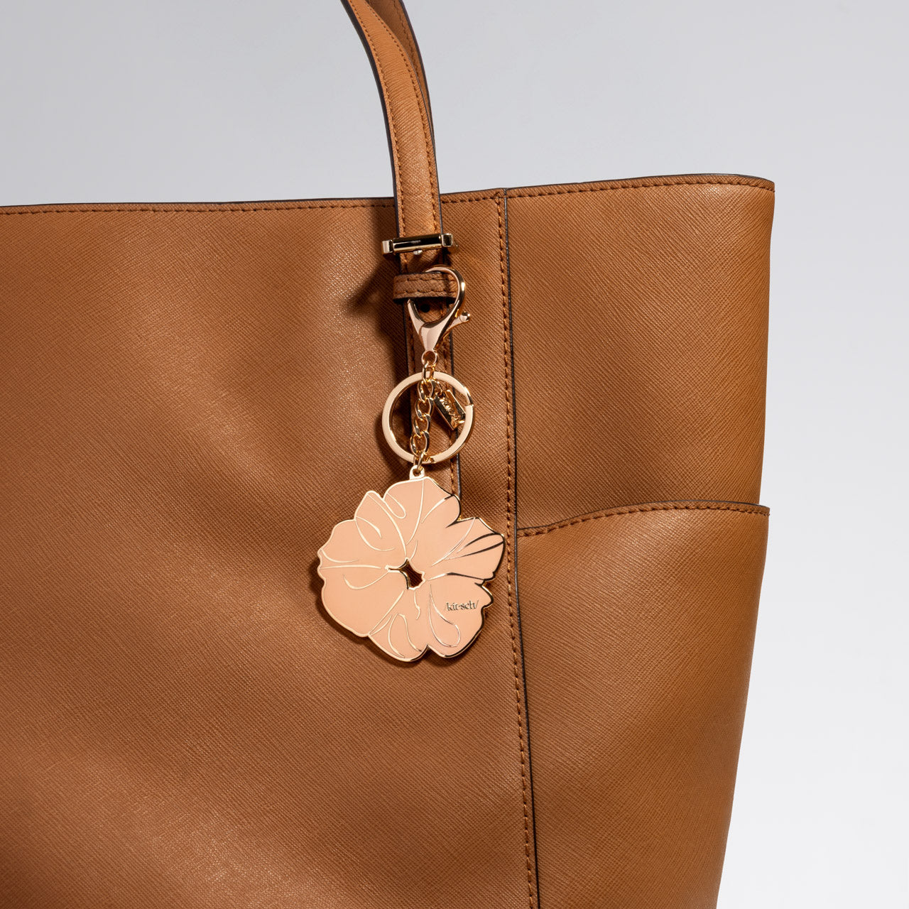 Brown leather handbag with a metal enamel keychain depicting the kitsch Terracotta Scrunchie with gold outline, design, and hardware on a light gray background
