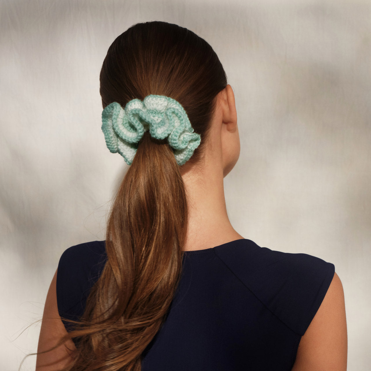 Person with a Kitsch Seafoam blue crochet scrunchie in their hair against a neutral background