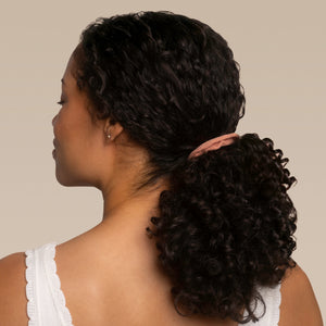 Woman with curly or coily hair in a ponytail using a kitsch terracotta petal hair elastic against a neutral background