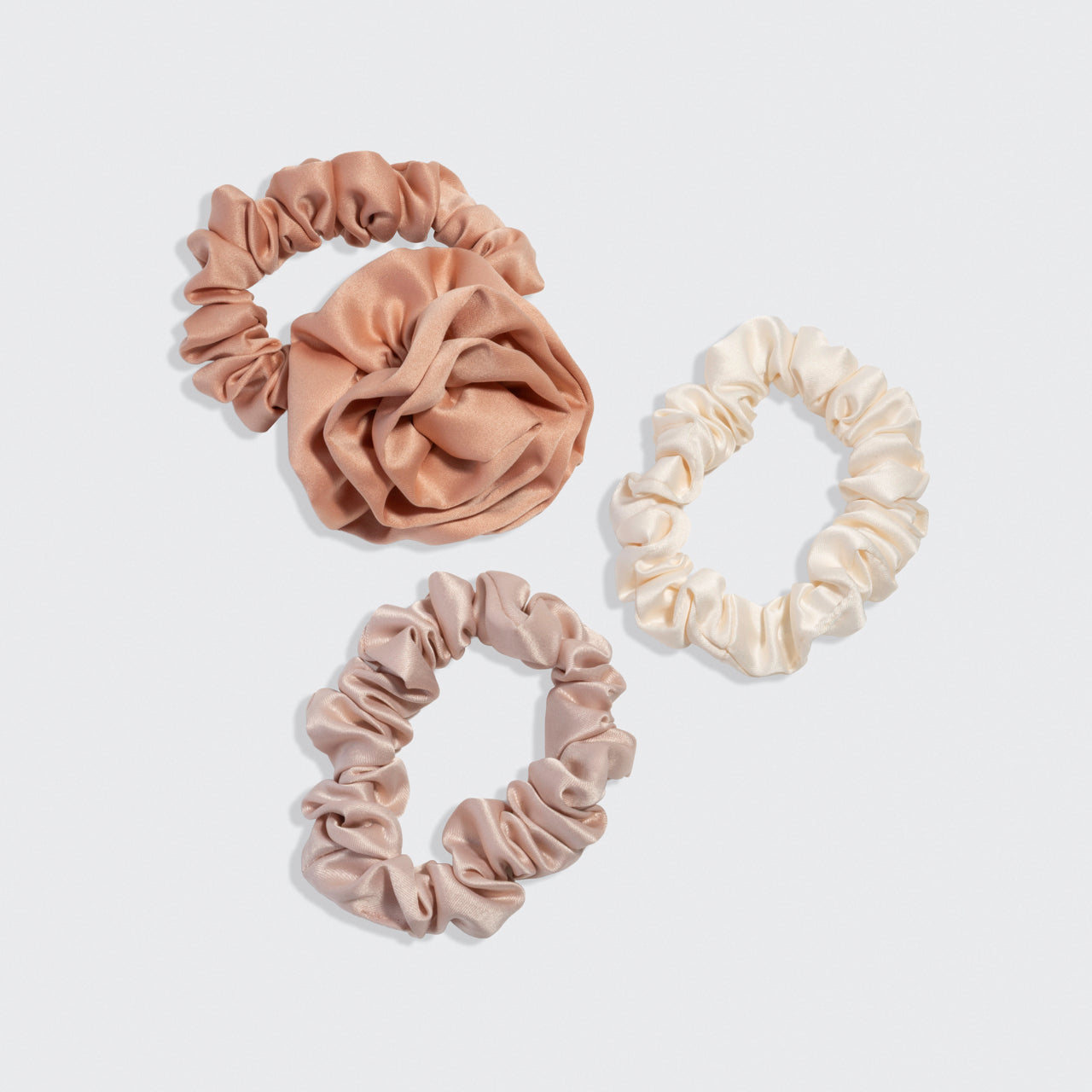 Set of three kitsch scrunchies in beige, terracotta, and cream colors on a light gray background.
